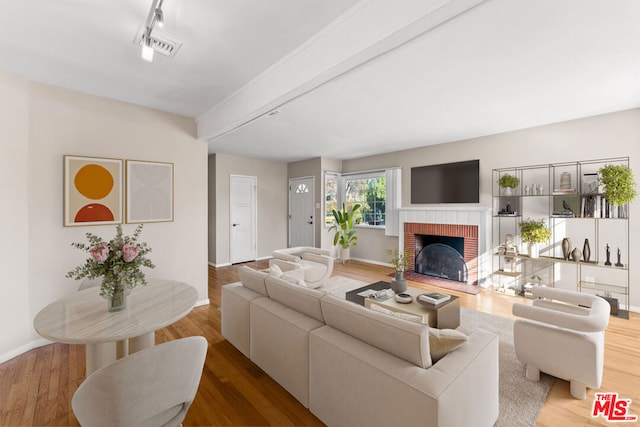 living room with beamed ceiling, wood-type flooring, a fireplace, and rail lighting