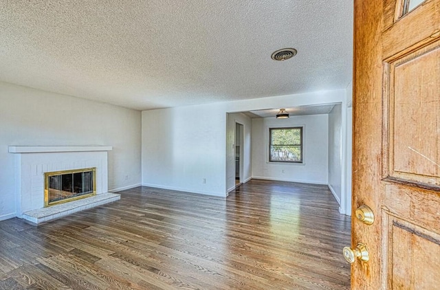 unfurnished living room featuring a textured ceiling, dark hardwood / wood-style flooring, and a brick fireplace