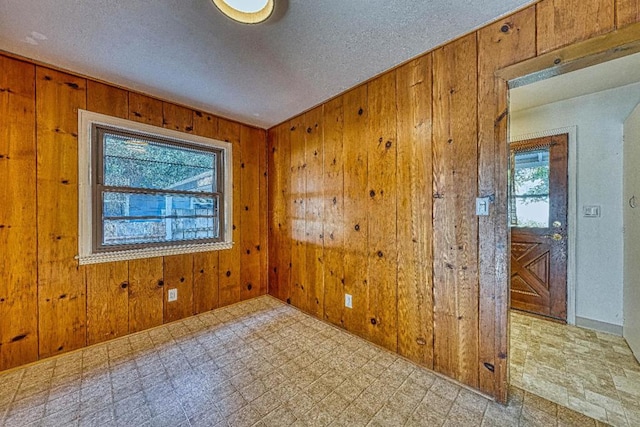 unfurnished room featuring a textured ceiling and wood walls