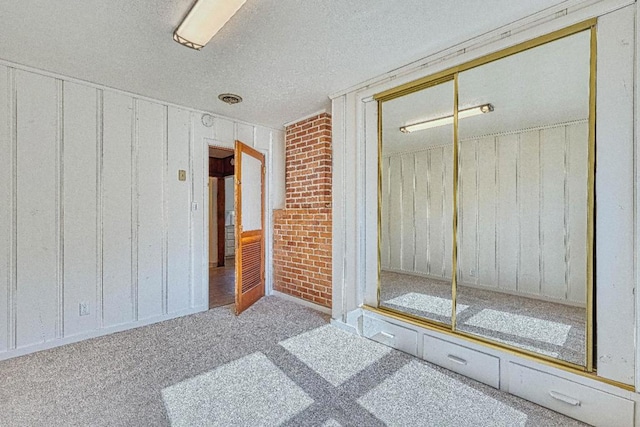 unfurnished room featuring brick wall, light carpet, and a textured ceiling