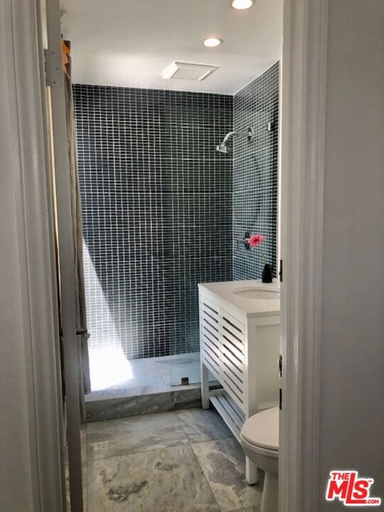 bathroom with a tile shower, vanity, and toilet