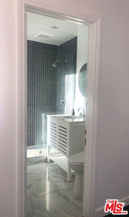 bathroom with vanity, toilet, and tiled shower