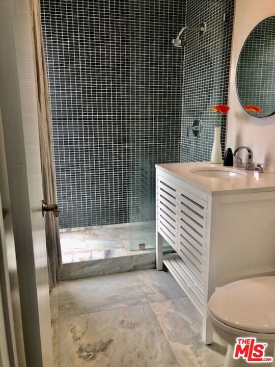 bathroom with vanity, toilet, and tiled shower