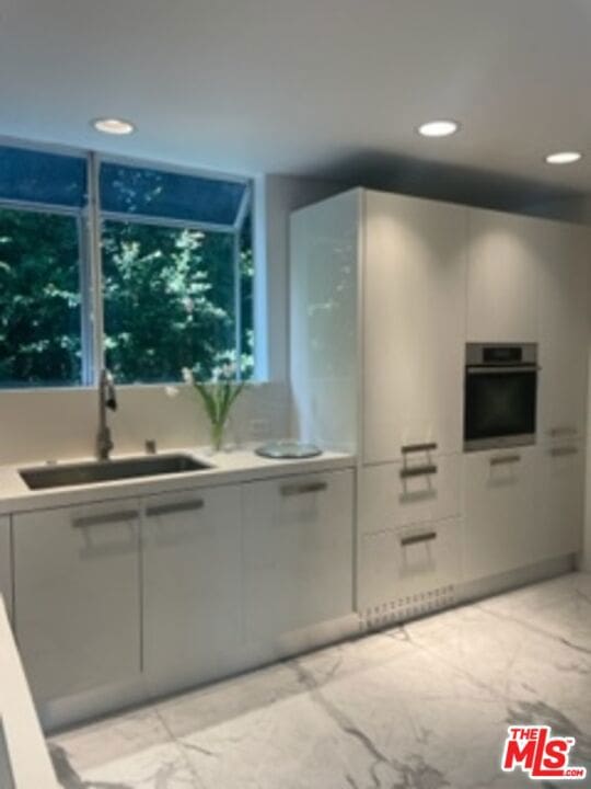 kitchen with stainless steel oven, white cabinetry, and sink