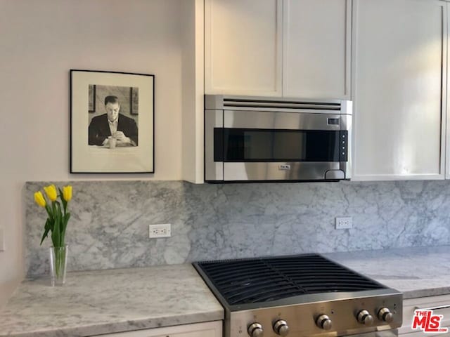 kitchen with light stone countertops, stainless steel appliances, white cabinetry, and tasteful backsplash