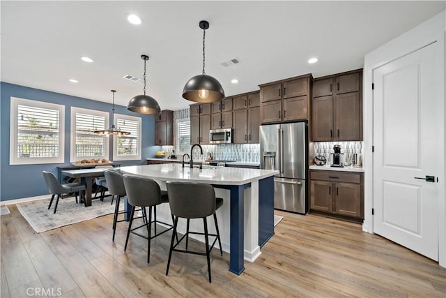 kitchen with stainless steel appliances, backsplash, light hardwood / wood-style floors, decorative light fixtures, and dark brown cabinets