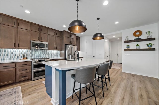 kitchen with a kitchen island with sink, light hardwood / wood-style floors, decorative light fixtures, and appliances with stainless steel finishes