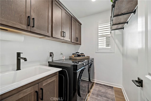 clothes washing area with cabinets, sink, washer and dryer, and hardwood / wood-style flooring