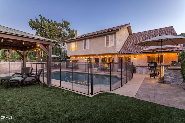 pool at dusk featuring a patio, a gazebo, an outdoor bar, and a lawn