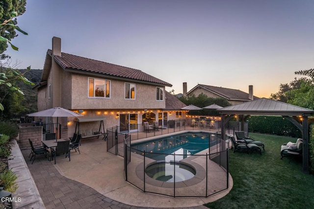 pool at dusk with a gazebo, a yard, an in ground hot tub, and a patio area