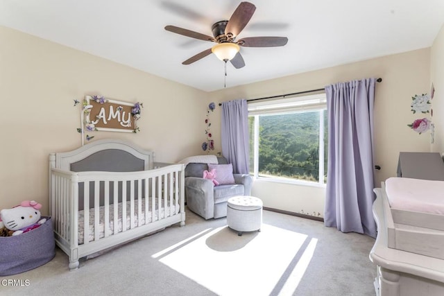 carpeted bedroom featuring a crib and ceiling fan