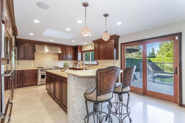 kitchen featuring tasteful backsplash, a skylight, appliances with stainless steel finishes, pendant lighting, and wall chimney range hood