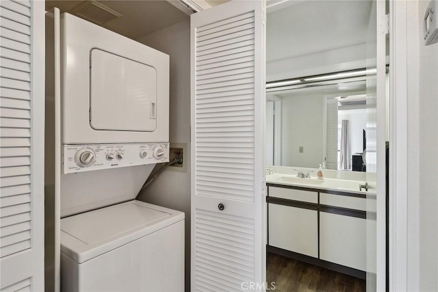 clothes washing area with sink, stacked washer / drying machine, and dark hardwood / wood-style flooring