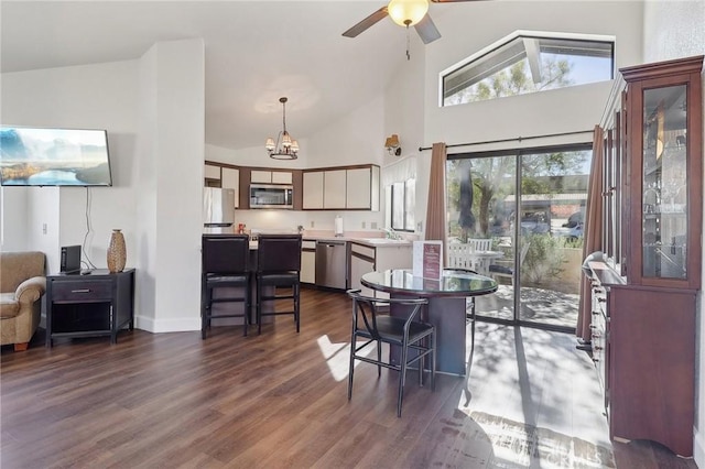 dining area with high vaulted ceiling, dark wood-type flooring, sink, and ceiling fan with notable chandelier