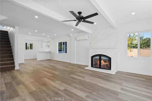 unfurnished living room with beamed ceiling, light hardwood / wood-style flooring, a wall unit AC, and a fireplace