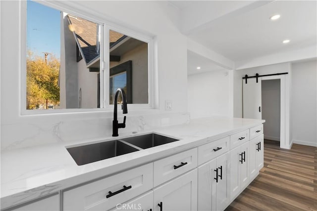 kitchen featuring sink, a barn door, light stone counters, dark hardwood / wood-style floors, and white cabinets