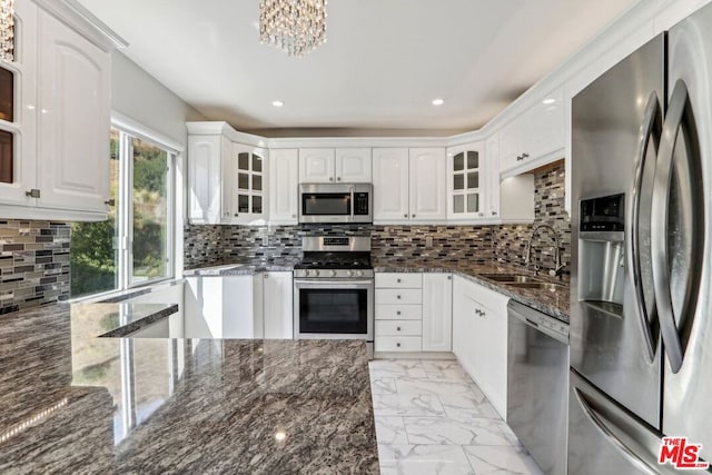 kitchen with appliances with stainless steel finishes, backsplash, dark stone counters, sink, and white cabinets