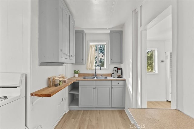 kitchen with gray cabinetry, butcher block counters, sink, light hardwood / wood-style flooring, and washer / clothes dryer