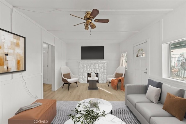 living room with ceiling fan, light hardwood / wood-style floors, and a stone fireplace