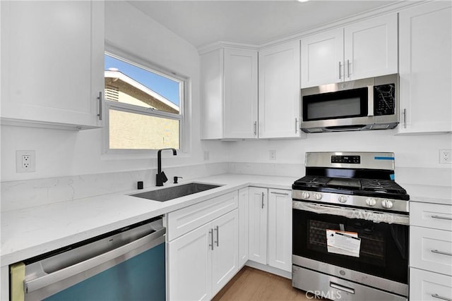 kitchen featuring sink, light hardwood / wood-style flooring, appliances with stainless steel finishes, light stone counters, and white cabinetry