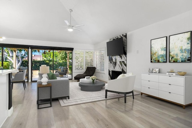 living room featuring ceiling fan, lofted ceiling, a premium fireplace, and light hardwood / wood-style flooring