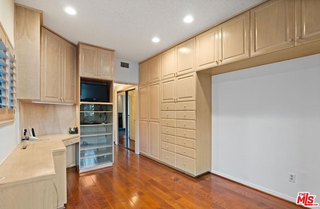 kitchen with a textured ceiling, built in desk, dark wood-type flooring, and light brown cabinetry