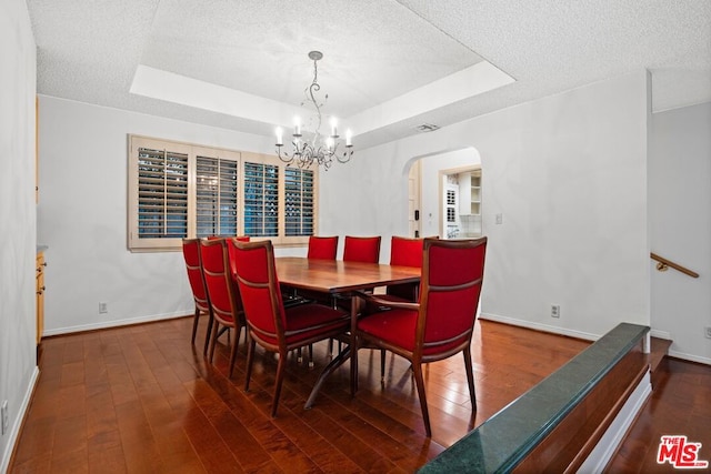 dining space with dark hardwood / wood-style flooring, a textured ceiling, a tray ceiling, and an inviting chandelier