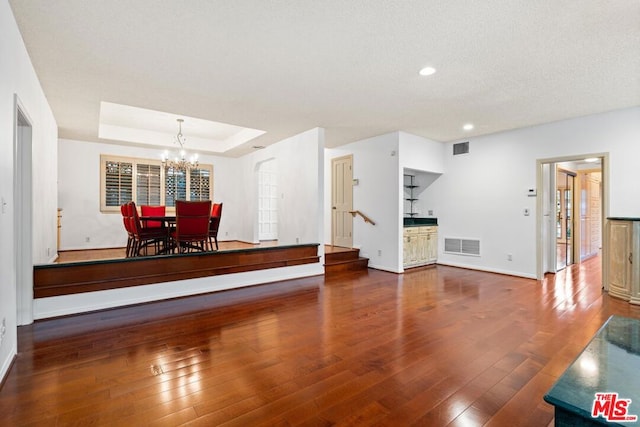 unfurnished living room with a chandelier, a textured ceiling, hardwood / wood-style flooring, and a raised ceiling