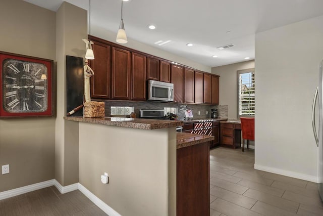 kitchen featuring kitchen peninsula, appliances with stainless steel finishes, backsplash, hanging light fixtures, and dark tile patterned floors