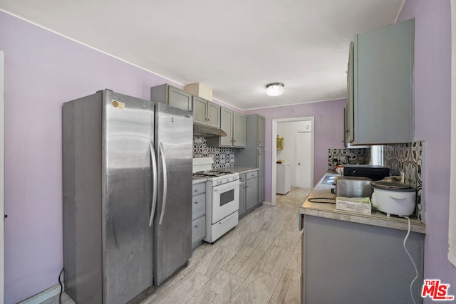 kitchen featuring decorative backsplash, white gas range oven, gray cabinetry, washer / clothes dryer, and stainless steel refrigerator