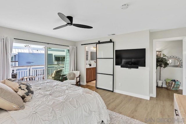 bedroom featuring ensuite bath, ceiling fan, a barn door, access to outside, and light wood-type flooring