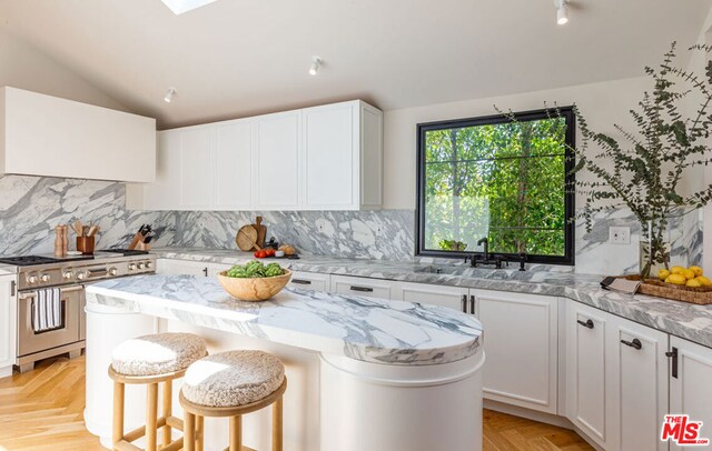 kitchen featuring range with two ovens, vaulted ceiling, light stone countertops, a kitchen island, and white cabinetry