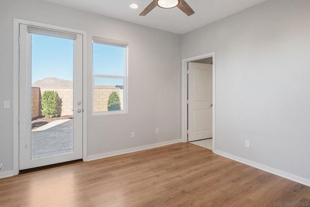 unfurnished room with a mountain view, light hardwood / wood-style floors, ceiling fan, and a healthy amount of sunlight