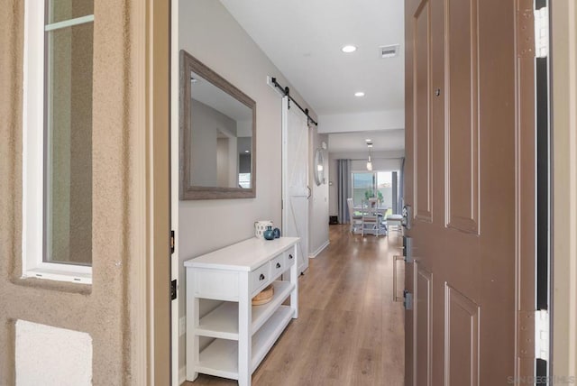 hall with a barn door and light hardwood / wood-style floors