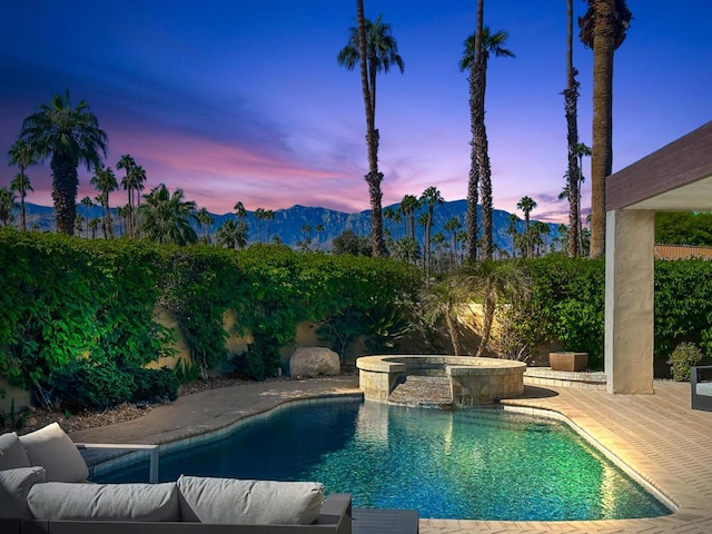 pool at dusk featuring a mountain view and an in ground hot tub