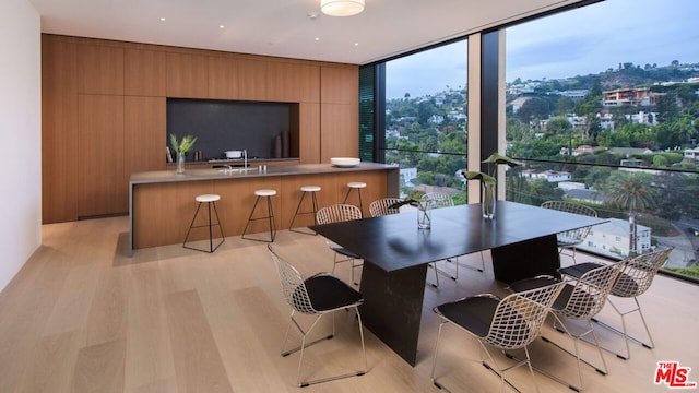 dining room with floor to ceiling windows, wooden walls, and light wood-type flooring