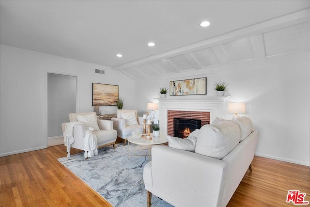 living room featuring a fireplace, light hardwood / wood-style flooring, and lofted ceiling with beams