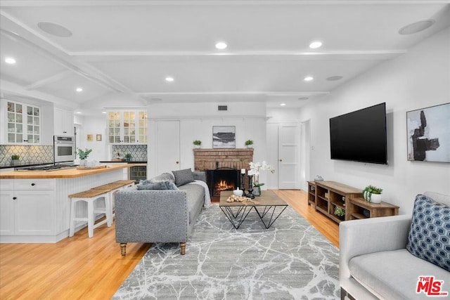 living room featuring beam ceiling, wine cooler, light hardwood / wood-style floors, and a brick fireplace