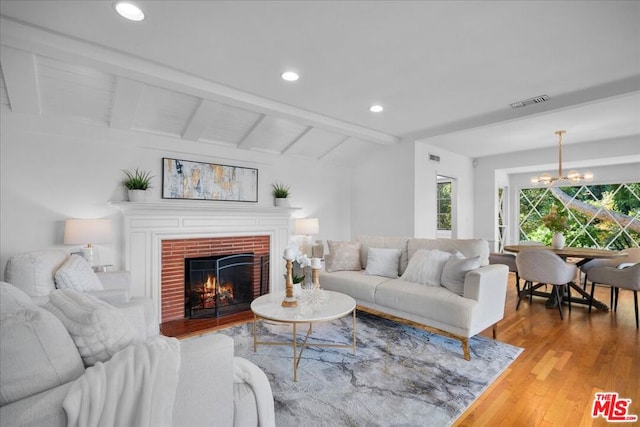 living room with a chandelier, vaulted ceiling with beams, hardwood / wood-style flooring, and a brick fireplace