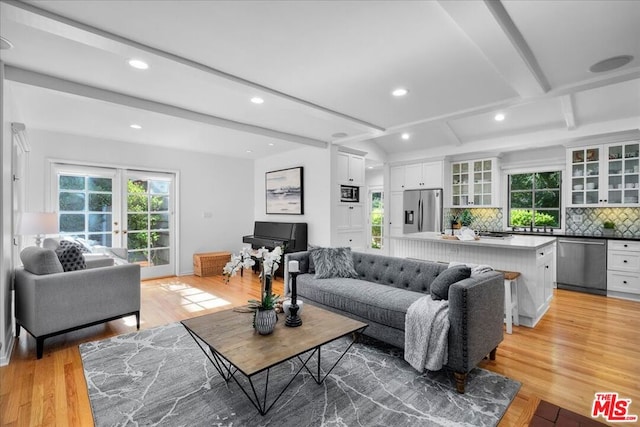 living room with beam ceiling, light hardwood / wood-style flooring, and french doors