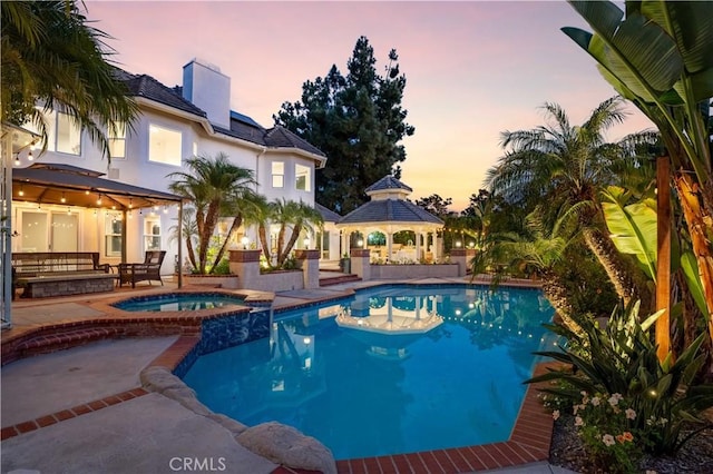 pool at dusk with an in ground hot tub, a gazebo, and a patio area