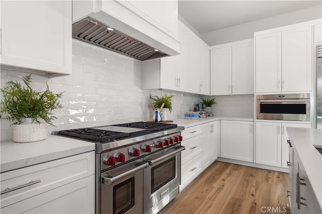 kitchen with white cabinets, custom range hood, light wood-type flooring, and stainless steel appliances