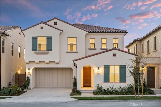 mediterranean / spanish-style home featuring a garage, driveway, a tiled roof, and stucco siding