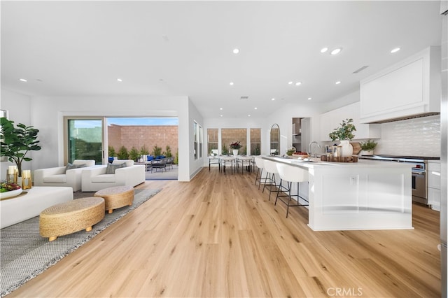 kitchen featuring light wood-style flooring, a breakfast bar, a spacious island, white cabinetry, and open floor plan