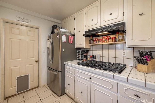 kitchen with backsplash, white cabinets, light tile patterned floors, tile counters, and stainless steel appliances