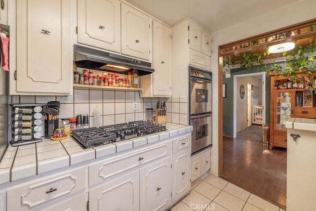 kitchen with white cabinets, appliances with stainless steel finishes, tile countertops, and light hardwood / wood-style floors