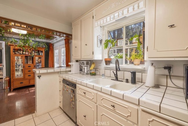 kitchen with dishwasher, sink, kitchen peninsula, tile countertops, and light wood-type flooring