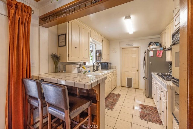 kitchen featuring tile countertops, crown molding, light tile patterned floors, a kitchen bar, and stainless steel appliances