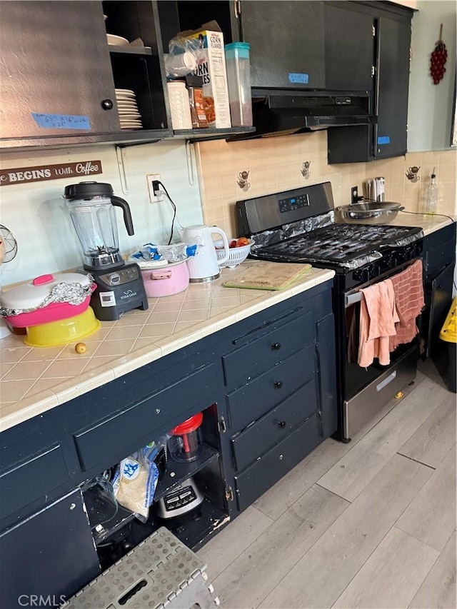 kitchen featuring tile countertops, stainless steel range with gas cooktop, light wood-type flooring, tasteful backsplash, and extractor fan