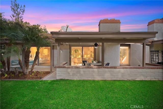 back house at dusk featuring a patio area, ceiling fan, and a yard